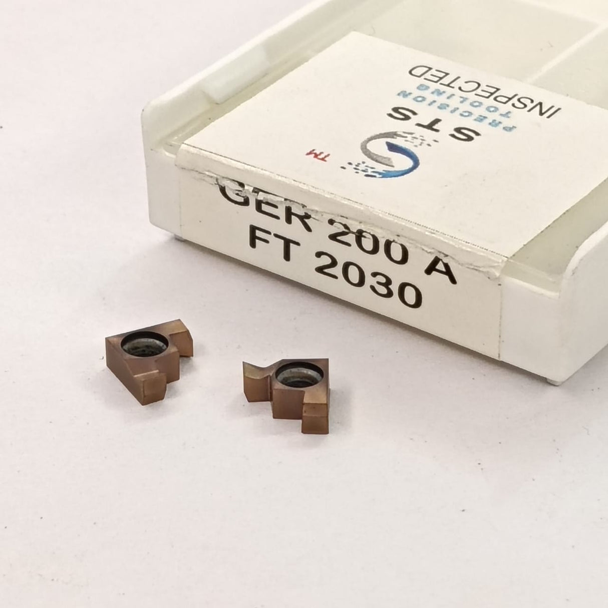 Two metal cutting inserts and a box labeled 'STS'
