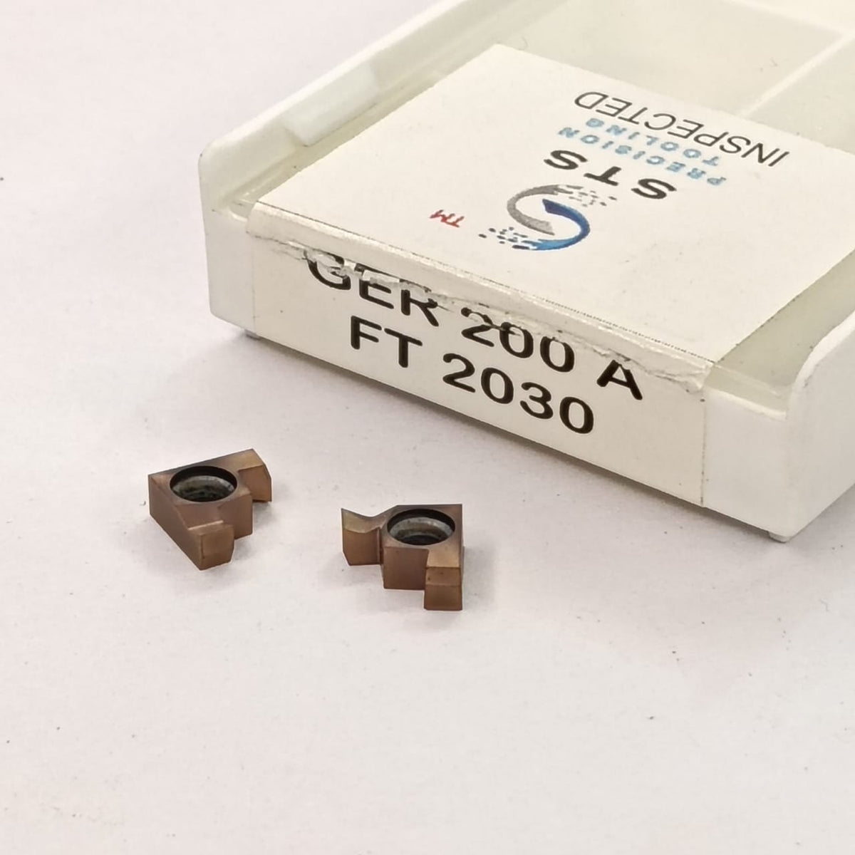 Two metal cutting inserts and a box labeled 'STS'